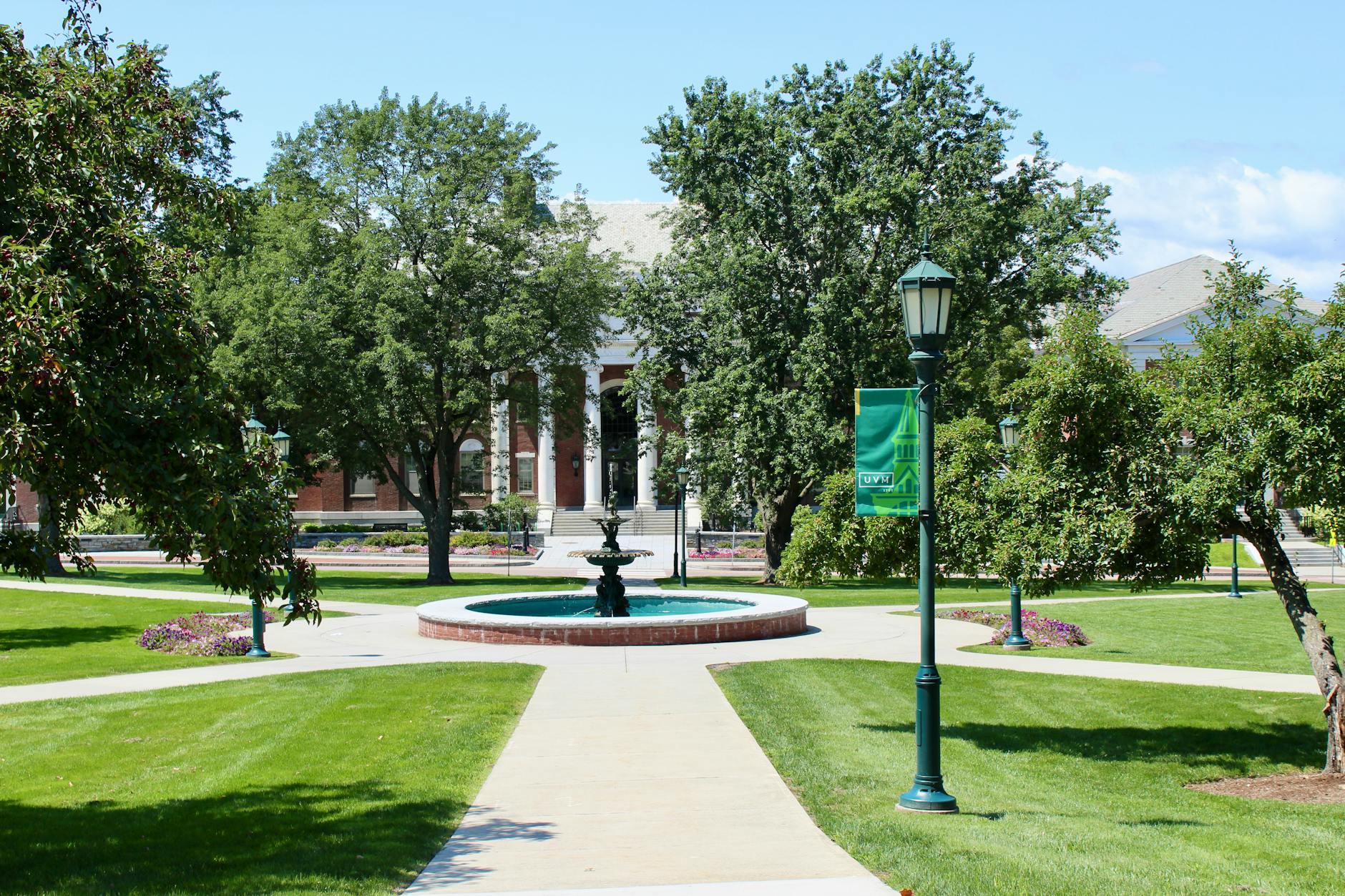 Sunny day on a university campus with a fountain and lush greenery.