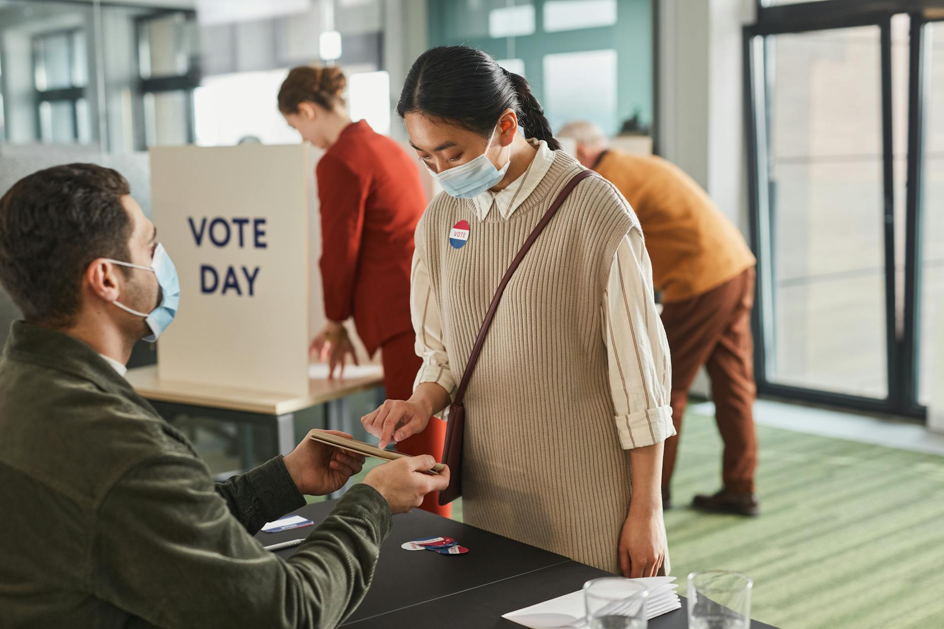 Voters casting ballots indoors on Election Day, wearing masks and using tablets for contactless voting.